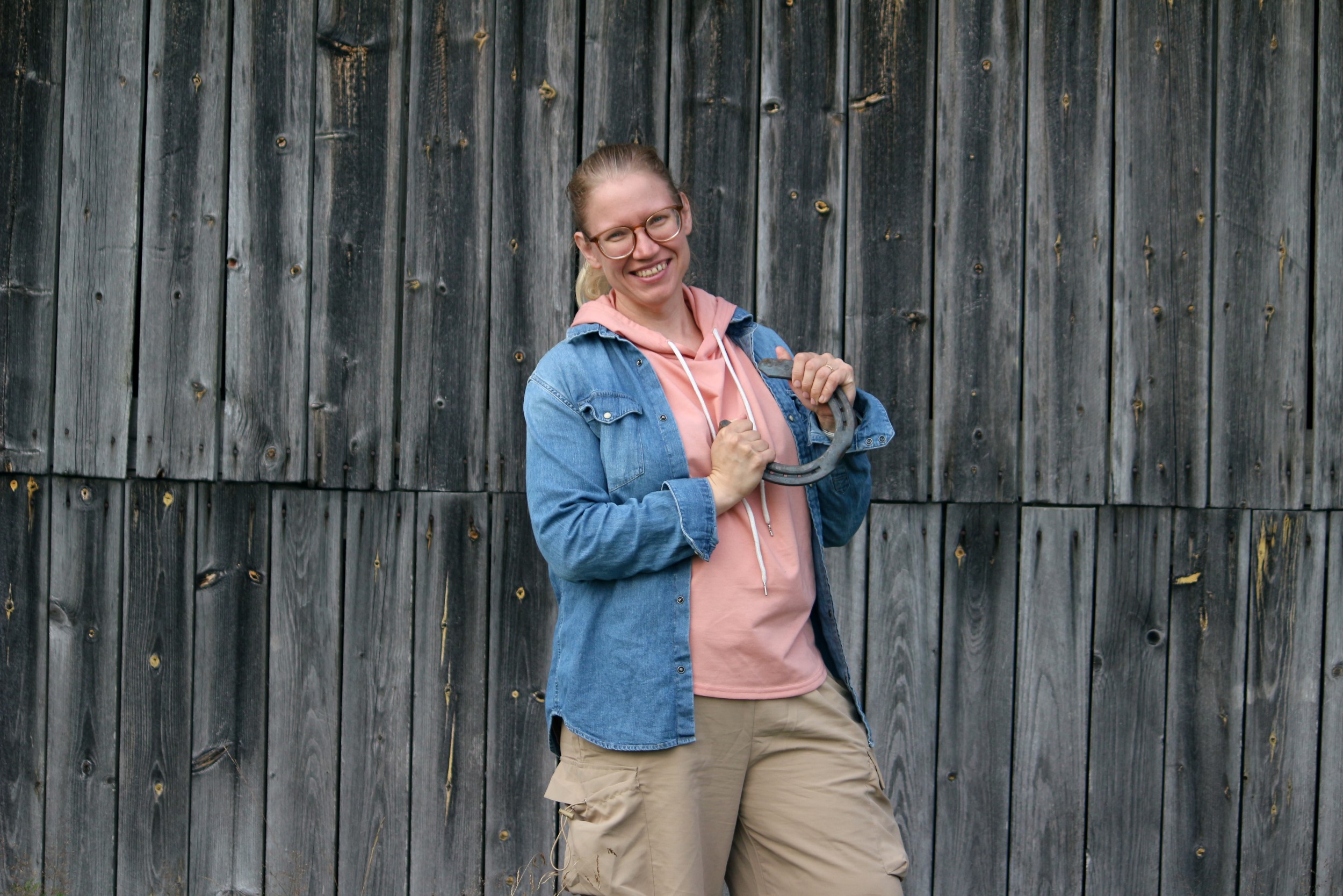 Hanna-Kaisa is standing in front of a barn wall holding a horseshoe